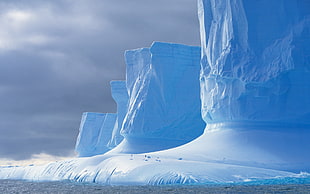 white icy mountain near body of water under dark clouds