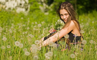 woman holding bunch of flowers sitting on flower field wearing black dress HD wallpaper