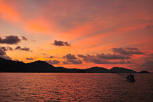 silhouette color of mountain with boat sailing under cloudy sky