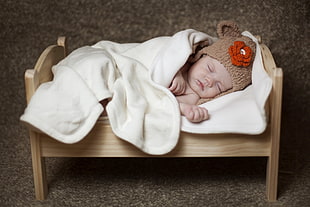 baby in brown knit critter cap laying on brown bed HD wallpaper
