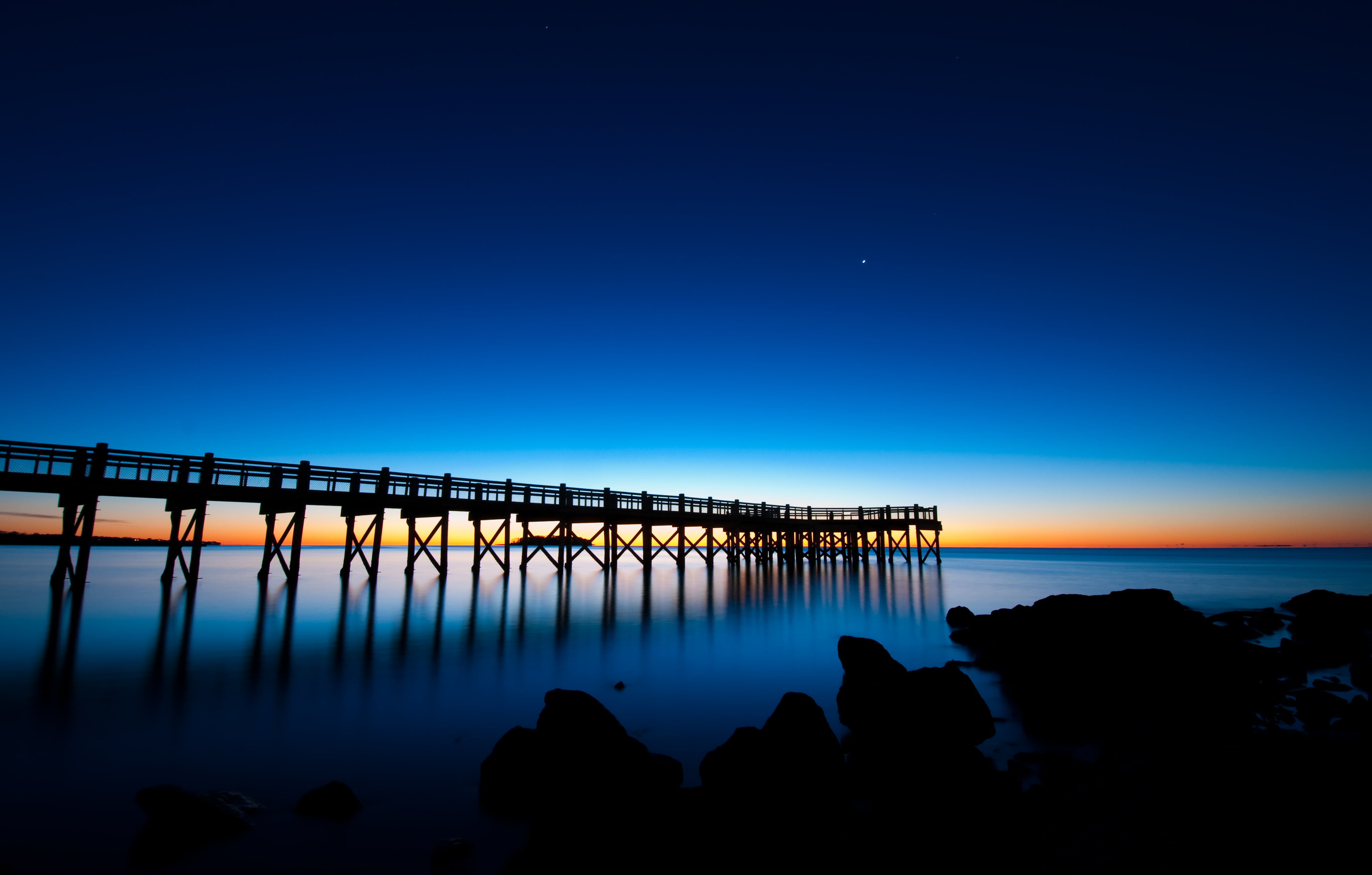 silhouette of wooden bridge on water at dawn