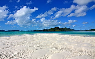 body of water near mountain under blue cloudy sky